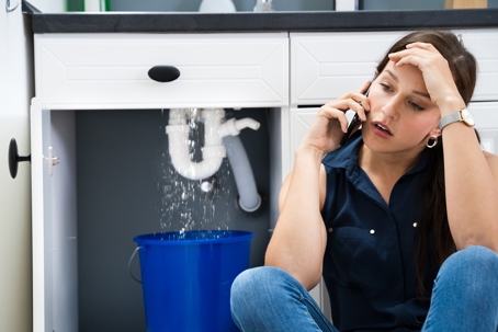 Lady on her phone with a leaking sink pipe behind her